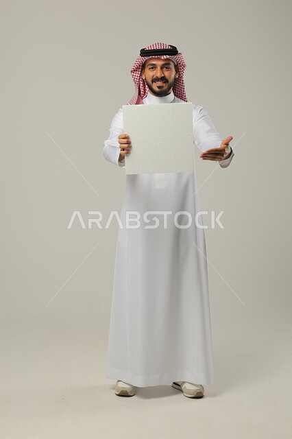  موك اب مربع أبيض, استخدام لوحات توضيحية ووسائل تعليمية، إعلانات وعروض تسويقية, بورتريه لرجل عربي خليجي سعودي مبتسم يرتدي الثوب التقليدي و الشماغ يشير بيده إلى لوحة بيضاء فارغة, صورة للجسم بالطول الكامل, خلفية رمادية