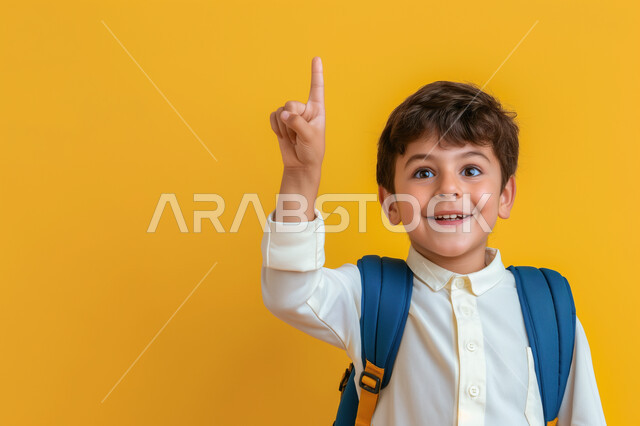 التفاعل والمشاركة داخل الفصل الدراسي، بورتريه مقرب لطالب عربي خليجي سعودي يرتدي الثوب التقليدي وحقيبة الظهر يرفع يده للأعلى للإجابة، التربية والتعليم بالمناهج المقررة للطلاب في المملكة العربية السعودية، خلفية صفراء