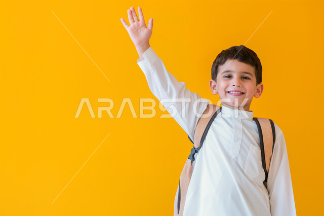 التفاعل والمشاركة داخل الفصل الدراسي، بورتريه مقرب لطالب عربي خليجي سعودي يرتدي الثوب التقليدي وحقيبة الظهر يرفع يده للأعلى للإجابة، التربية والتعليم بالمناهج المقررة للطلاب في المملكة العربية السعودية، خلفية صفراء
