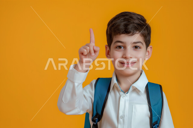 التفاعل والمشاركة داخل الفصل الدراسي، بورتريه مقرب لطالب عربي خليجي سعودي يرتدي الثوب التقليدي وحقيبة الظهر يرفع يده للأعلى للإجابة، التربية والتعليم بالمناهج المقررة للطلاب في المملكة العربية السعودية، خلفية صفراء