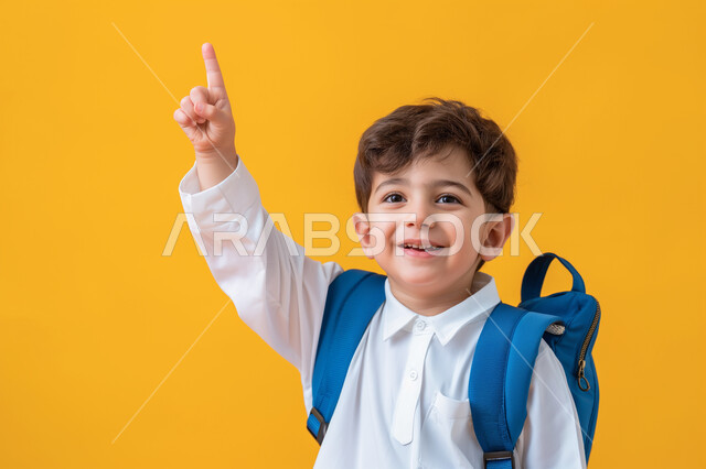 التفاعل والمشاركة داخل الفصل الدراسي، بورتريه مقرب لطالب عربي خليجي سعودي يرتدي الثوب التقليدي وحقيبة الظهر يرفع يده للأعلى للإجابة، التربية والتعليم بالمناهج المقررة للطلاب في المملكة العربية السعودية، خلفية صفراء