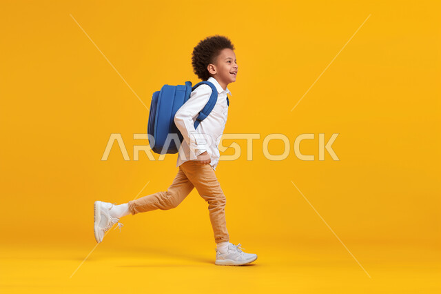 الجد والاجتهاد والنشاط الصباحي، بورتريه لولد عربي خليجي سعودي يرتدي الحقيبة المدرسية يقوم بالذهاب الى المدرسة، بدء الدوام الصباحي في مدارس المملكة العربية السعودية، صورة الجسم بالكامل، خلفية صفراء