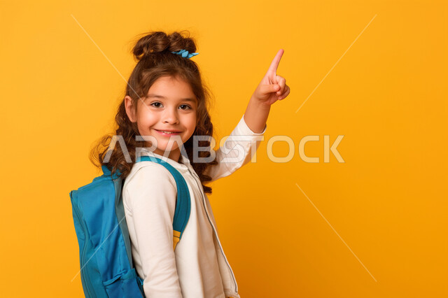 المشاركة والتفاعل داخل الفصل الدراسي، بورتريه مقرب لطالبة عربية خليجية سعودية ترتدي حقيبة الظهر ترفع يدها للأعلى للإجابة، التربية والتعليم بالمناهج المقررة للطلاب في المملكة العربية السعودية، خلفية صفراء