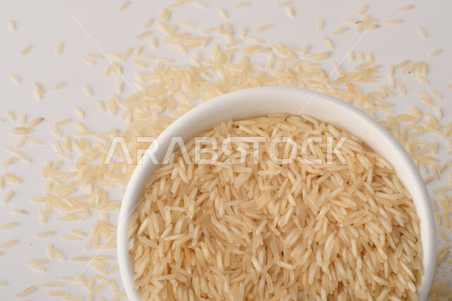 طبق أبيض مليء بحبيبات الرز ، الرز الابيض ،محصول الارز على خلفية بيضاء ، محاصيل زراعية