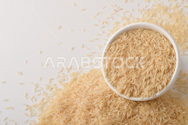 طبق أبيض مليء بحبيبات الرز ، الرز الابيض ،محصول الارز على خلفية بيضاء ، محاصيل زراعية