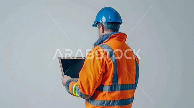 Integrating work with technology, studying the basics of the project through modern applications and technologies, engineering project management, close-up portrait from the back of a Saudi Gulf Arab engineer wearing a helmet and protective vest holding a laptop in his hand, gray background
