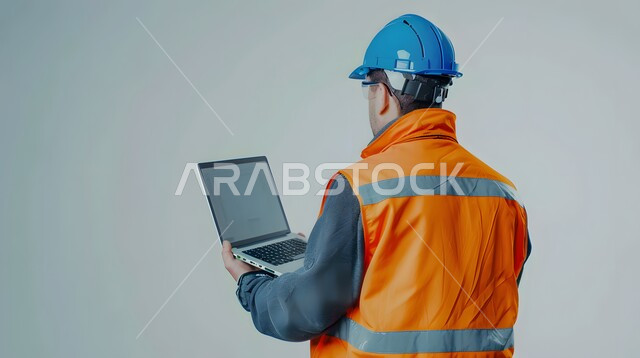 Studying the basics of the project through modern applications and technologies, integrating work with technology, engineering project management, close-up portrait from the back of a Saudi Gulf Arab engineer wearing a helmet and protective vest holding a laptop in his hand, gray background
