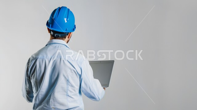  إدارة المشاريع الهندسية، دمج العمل مع التكنولوجيا, دراسة أساسيات المشروع عبر التطبيقات والتقنيات الحديثة, بورتريه مقرب من الخلف لمهندس عربي خليجي سعودي يرتدي الخوذة وسترة الحماية يمسك بيده جهاز الحاسوب المحمول, خلفية رمادية
