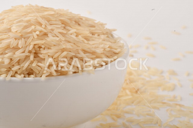 طبق أبيض مليء بحبيبات الرز ، الرز الابيض ،محصول الارز على خلفية بيضاء ، محاصيل زراعية