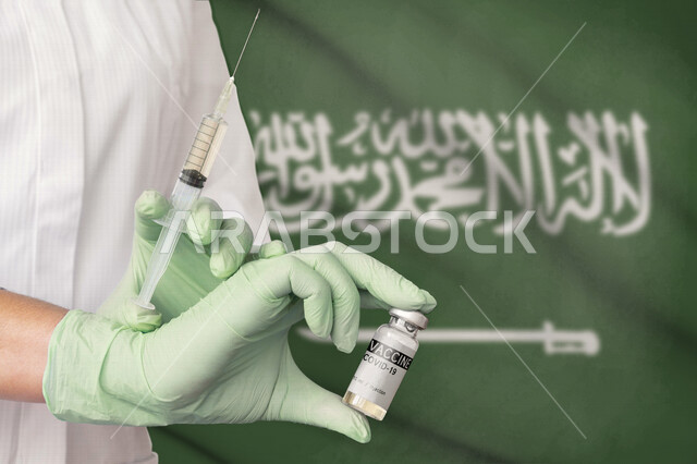 A Saudi Arabian Gulf doctor holding the vaccine and the medical syringe in his hand, wearing medical gloves, preparing a safe vaccine dose, safe vaccination for covid 19, medical vaccination, a dose to avoid infection, background with the flag of the King
