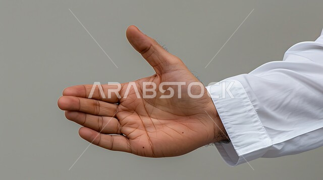 مفهوم الاستقبال والترحيب، التعارف و الصداقه وتكوين علاقات, إلقاء التحيه والسلام, بورتريه مقرب ليد رجل عربي خليجي سعودي يرتدي الثوب التقليدي يقوم برفع كفه, خلفية رمادية