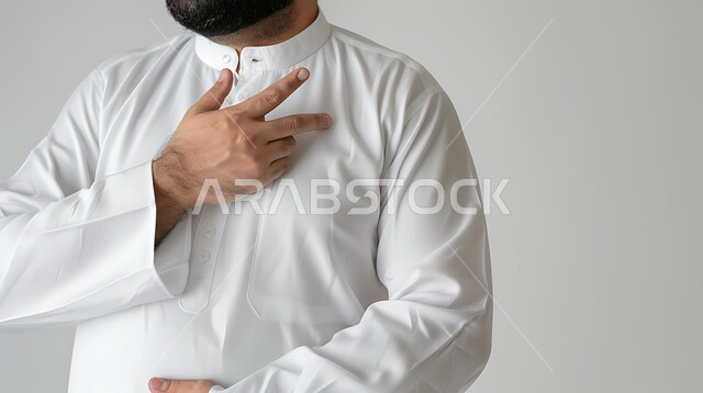التعب والإرهاق والضغوطات النفسية، اضطرابات وأمراض قلبية, الشعور في زيادة معدل ضربات القلب, الاحساس بذبحه صدريه، بورتريه مقرب لرجل عربي خليجي سعودي يرتدي الثوب التقليدي يضع يده على صدره يشعر بحالة سيئة، خلفية بيضاء