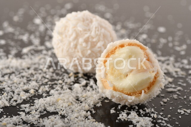 كرات حلوى الشوكولاته البيضاء مُكونة من اللوز والجوز الهند , صورة مقربة لحلوى متشققة مع رقائق اللوز وجوز الهند اللذيذة على طاولة سوداء