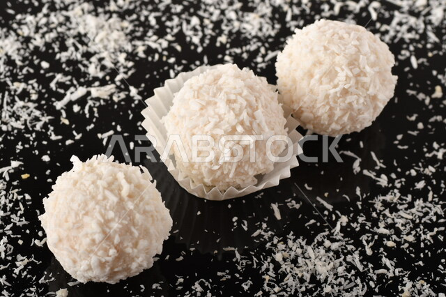 كرات حلوى الشوكولاته البيضاء مُكونة من اللوز والجوز الهند , صورة مقربة لحلوى متشققة مع رقائق اللوز وجوز الهند اللذيذة على طاولة سوداء