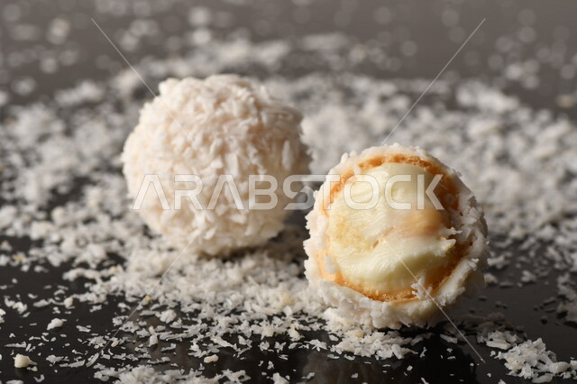 كرات حلوى الشوكولاته البيضاء مُكونة من اللوز والجوز الهند , صورة مقربة لحلوى متشققة مع رقائق اللوز وجوز الهند اللذيذة على طاولة سوداء