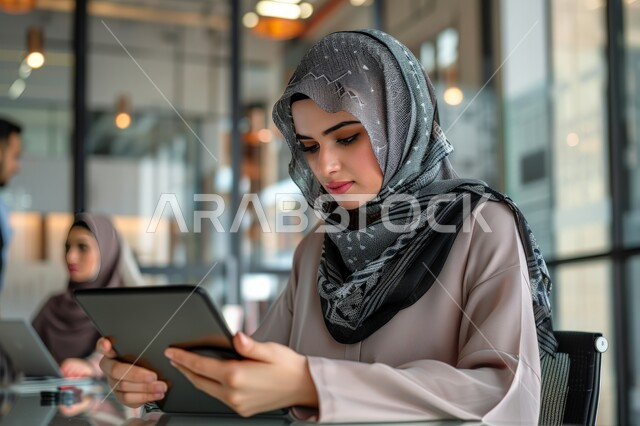 Using modern and advanced technical means to accomplish tasks, managing and organizing business at the company's headquarters, a comfortable work environment in the Kingdom's companies, women's office jobs and professions, a veiled Saudi Arabian Gulf woman working on a tablet in the office