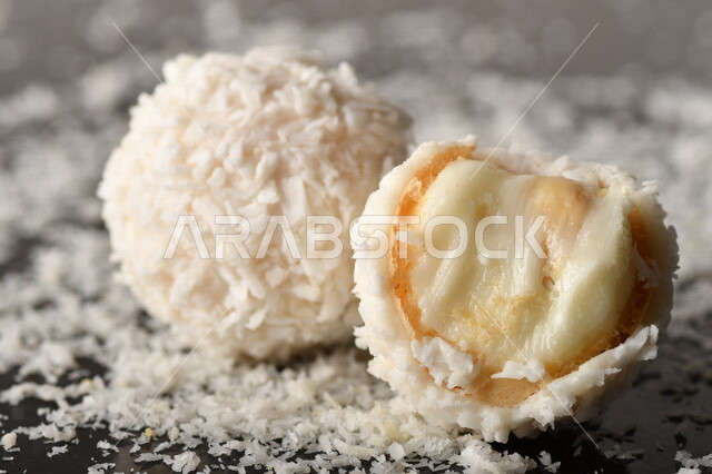 كرات حلوى الشوكولاته البيضاء مُكونة من اللوز والجوز الهند , صورة مقربة لحلوى متشققة مع رقائق اللوز وجوز الهند اللذيذة على طاولة سوداء