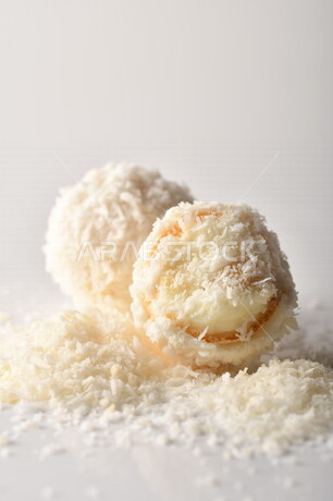 كرات حلوى الشوكولاته البيضاء مُكونة من اللوز والجوز الهند , صورة مقربة لحلوى متشققة مع رقائق اللوز وجوز الهند اللذيذة على طاولة بيضاء , خلفية بيضاء