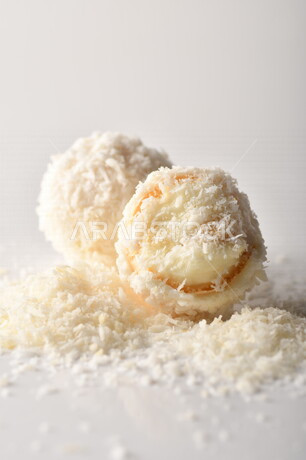 كرات حلوى الشوكولاته البيضاء مُكونة من اللوز والجوز الهند , صورة مقربة لحلوى متشققة مع رقائق اللوز وجوز الهند اللذيذة على طاولة بيضاء , خلفية بيضاء