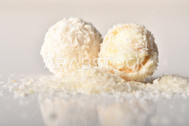 كرات حلوى الشوكولاته البيضاء مُكونة من اللوز والجوز الهند , صورة مقربة لحلوى متشققة مع رقائق اللوز وجوز الهند اللذيذة على طاولة بيضاء , خلفية بيضاء