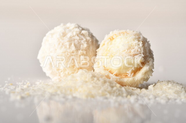 كرات حلوى الشوكولاته البيضاء مُكونة من اللوز والجوز الهند , صورة مقربة لحلوى متشققة مع رقائق اللوز وجوز الهند اللذيذة على طاولة بيضاء , خلفية بيضاء