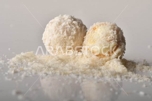 كرات حلوى الشوكولاته البيضاء مُكونة من اللوز والجوز الهند , صورة مقربة لحلوى متشققة مع رقائق اللوز وجوز الهند اللذيذة على طاولة بيضاء , خلفية بيضاء