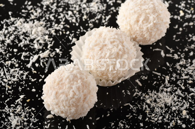 كرات حلوى الشوكولاته البيضاء مُكونة من اللوز والجوز الهند , صورة مقربة لحلوى متشققة مع رقائق اللوز وجوز الهند اللذيذة على طاولة سوداء