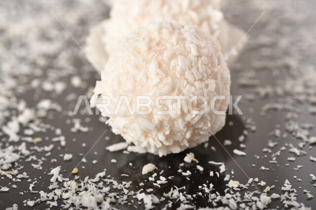 كرات حلوى الشوكولاته البيضاء مُكونة من اللوز والجوز الهند , صورة مقربة لحلوى متشققة مع رقائق اللوز وجوز الهند اللذيذة على طاولة سوداء