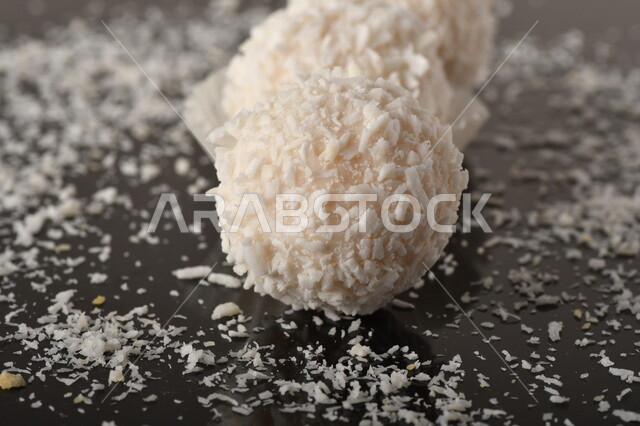 كرات حلوى الشوكولاته البيضاء مُكونة من اللوز والجوز الهند , صورة مقربة لحلوى متشققة مع رقائق اللوز وجوز الهند اللذيذة على طاولة سوداء