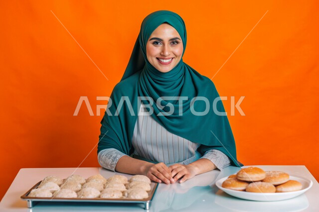 إعداد الحلويات بمكونات طبيعية طازجة، مهارات وفنون الطبخ, بورتريه مقرب لإمرأة عربية خليجية سعودية محجبة مبتسمة تنظر الى الكاميرا تقف داخل المطبخ تقوم بتحضير وصفات الطعام بإيماءات السرور والسعادة، خلفية ملونة
