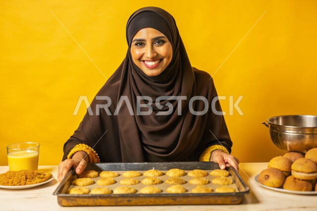 إعداد الحلويات بمكونات طبيعية طازجة، مهارات وفنون الطبخ, بورتريه مقرب لإمرأة عربية خليجية سعودية محجبة مبتسمة تنظر الى الكاميرا تقف داخل المطبخ تقوم بتحضير وصفات الطعام بإيماءات السرور والسعادة، خلفية ملونة