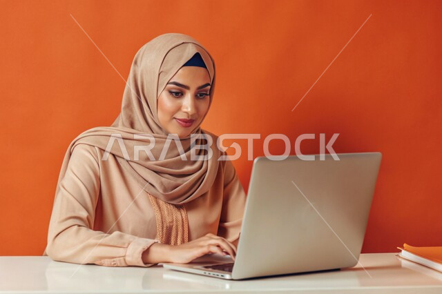 إستخدام الأجهزة التقنية الحديثة، مفهوم التعليم و العمل عن بعد، بورتريه مقرب لشابة عربية خليجية سعودية محجبة مبتسمة تعمل على جهاز الحاسوب المحمول، التسويق الإلكتروني وتصفح الإنترنت، مشاهدة الأفلام عبر اللابتوب، مهن ووظائف نسائية، خلفية ملونة