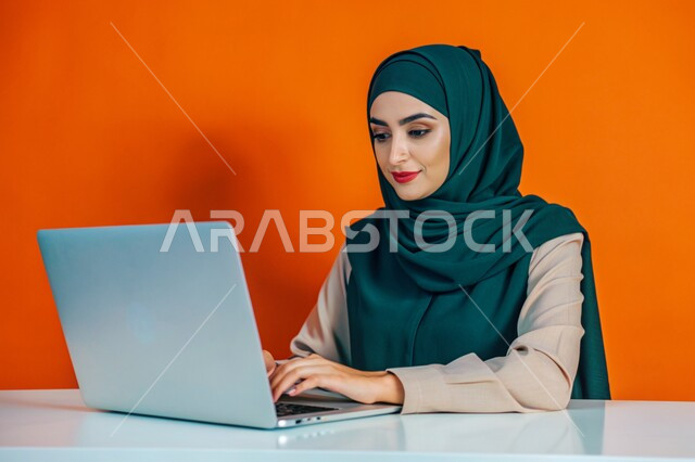 The use of modern technical devices, the concept of distance education and work, a close-up portrait of a smiling veiled Saudi Arabian Gulf woman working on a laptop, electronic marketing and Internet browsing, watching movies on the laptop, women’s professions and jobs, a colorful background