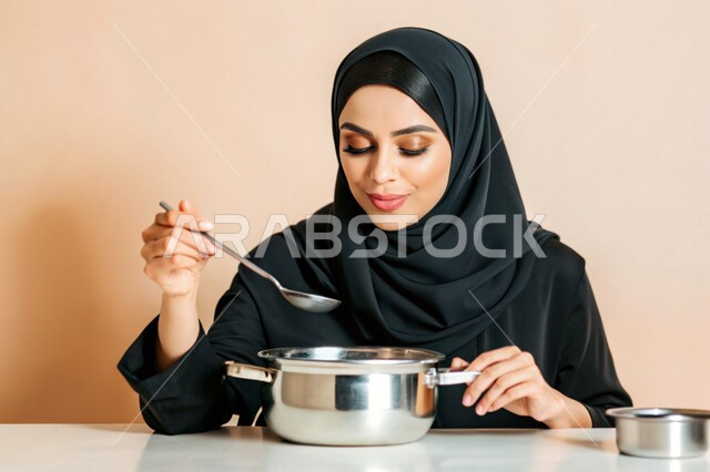 مهارات وفنون الطبخ, إعداد الأطعمة بمكونات طبيعية طازجة، بورتريه مقرب لإمرأة عربية خليجية سعودية محجبة مبتسمة تقوم بتذوق النكهات بإيماءات السرور والسعادة، تحضير وصفات الطعام، خلفية ملونة