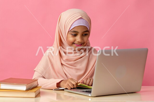 إستخدام الأجهزة التقنية الحديثة، مفهوم التعليم و العمل عن بعد، بورتريه مقرب لفتاة عربية خليجية سعودية محجبة مبتسمة تعمل على جهاز الحاسوب المحمول، جودة التعليم وتطور الوسائل التعليمية في المملكة العربية السعودية، خلفية وردية