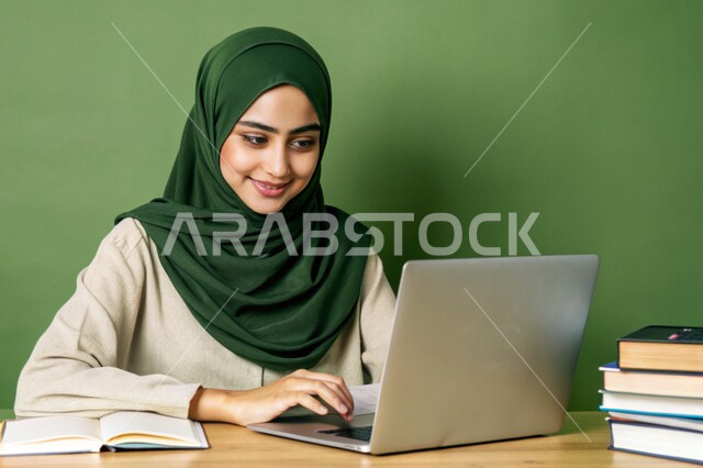 جودة التعليم وتطور الوسائل التعليمية في المملكة العربية السعودية، إستخدام الأجهزة التقنية الحديثة، مفهوم التعليم و العمل عن بعد، بورتريه مقرب لفتاة عربية خليجية سعودية محجبة مبتسمة تعمل على جهاز الحاسوب المحمول، خلفية خضراء