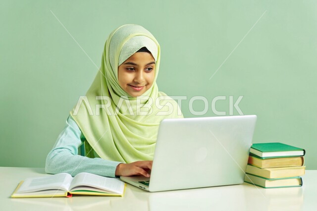 The quality of education and the development of educational methods in the Kingdom of Saudi Arabia, the use of modern technical devices, the concept of distance education and work, a close-up portrait of a veiled Saudi Arabian Gulf girl, smiling, working on a laptop, green background
