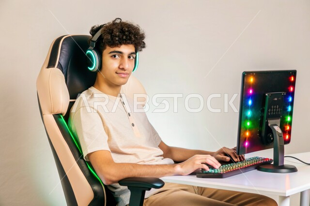منصة البث المباشر في عالم ألعاب الفيديو، بورتريه لشاب عربي خليجي سعودي يرتدي سماعة الرأس ينظر الى الكاميرا يعمل على جهاز الحاسوب المحمول، استخدام التقنيات والتكنولوجيا الحديثة، مفهوم الاندماج والتفاعل، خلفية بيضاء