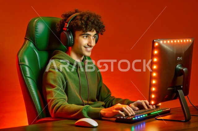 استخدام التقنيات والتكنولوجيا الحديثة، منصة البث المباشر في عالم ألعاب الفيديو، بورتريه لشاب عربي خليجي سعودي يرتدي سماعة الرأس يعمل على جهاز الحاسوب المحمول، مفهوم الاندماج والتفاعل، خلفية ملونة