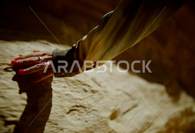 الاستمتاع بقضاء الأوقات في العطلة، الرحلات والمغامرات السياحية الممتعة, التكوينات والتشكيلات الصخرية في الصحراء, البيئة الصحراوية في المملكة العربية السعودية, صورة مقربة ليد إمرأة عربية خليجية سعودية ترتدي تقوم بلمس الصخور والأثار التاريخية