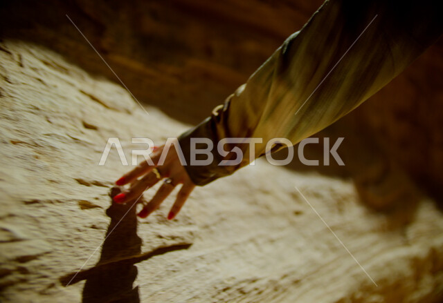 المغامرات والرحلات السياحية الممتعة, التكوينات والتشكيلات الصخرية في الصحراء, البيئة الصحراوية في المملكة العربية السعودية, صورة مقربة ليد إمرأة عربية خليجية سعودية ترتدي تقوم بلمس الصخور والأثار التاريخية، الاستمتاع بقضاء الأوقات في العطلة