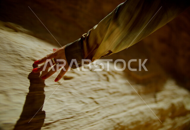 التكوينات والتشكيلات الصخرية في الصحراء, البيئة الصحراوية في المملكة العربية السعودية, أماكن المغامرات والرحلات السياحية الممتعة, صورة مقربة ليد إمرأة عربية خليجية سعودية ترتدي تقوم بلمس الصخور والأثار التاريخية، الاستمتاع بقضاء الأوقات في العطلة