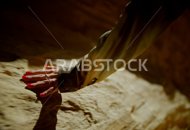 التشكيلات والتكوينات الصخرية في الصحراء, البيئة الصحراوية في المملكة العربية السعودية, أماكن المغامرات والرحلات السياحية الممتعة, صورة مقربة ليد إمرأة عربية خليجية سعودية ترتدي تقوم بلمس الصخور والأثار التاريخية، الاستمتاع بقضاء الأوقات في العطلة