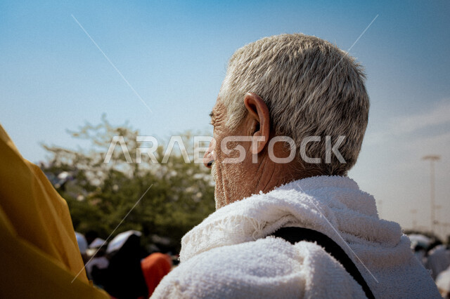 العبادة والتقرب إلى الله بالأعمال الصالحة، صورة مقربة من الخلف لرجل كبير السن خليجي عربي سعودي يرتدي ملابس الاحرام يقف على جبل عرفات، آداء مناسك الحج والعمرة، أماكن ومعالم دينية اسلامية مقدسة في المملكة العربية السعودية