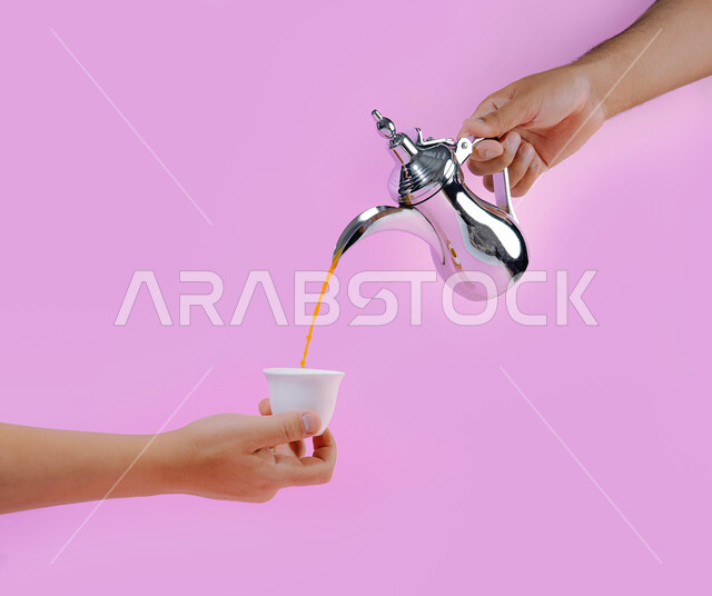 دلة فضية من البن العربي الفاخر, بورتريه لمقرب ليدي رجل عربي خليجي سعودي يقوم بصب مشروب القهوة في فنجان، مفهوم حسن استقبال الضيف وإكرامه, تقديم مشروب البن الساخن للزوار, العادات الأصيلة المتوارثة عند العرب, خلفية وردية