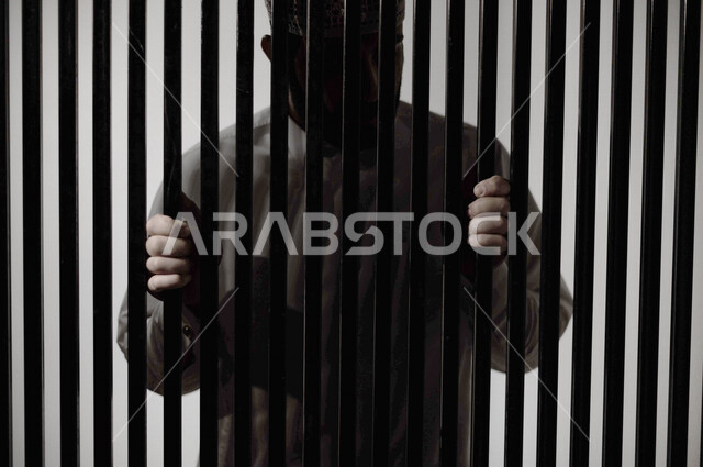 رجل عربي خليجي سعودي داخل السجن ، يمسك القضبان الحديدية ، سجين سعودي ينتظر الحرية ، الشعور بالندم والوحدة 