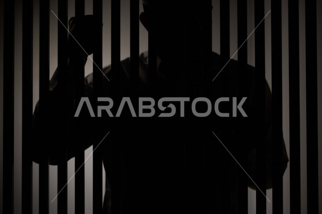 رجل عربي خليجي سعودي داخل السجن ، يمسك القضبان الحديدية ، سجين سعودي ينتظر الحرية ، الشعور بالندم والوحدة 