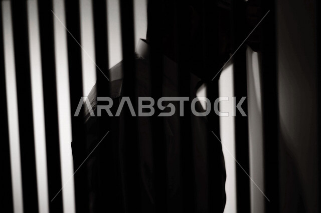 تصوير مقرب لرجل عربي خليجي سعودي ، خلف القضبان الحديدية ، سجين سعودي يضع راسه على الحائط ، الشعور بالندم والكابة ، انتظار الحرية 