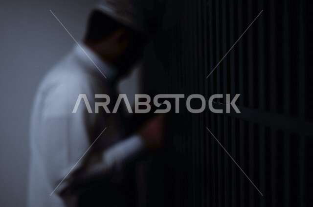 تصوير مقرب لرجل عربي خليجي سعودي ، خلف القضبان الحديدية ، سجين سعودي يضع قبضة يده على القضبان ، الشعور بالندم والوحدة، ينتظر الحرية 
