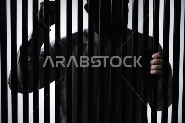 رجل عربي خليجي سعودي داخل السجن ، يمسك القضبان الحديدية ، سجين سعودي ينتظر الحرية ، الشعور بالندم والوحدة 